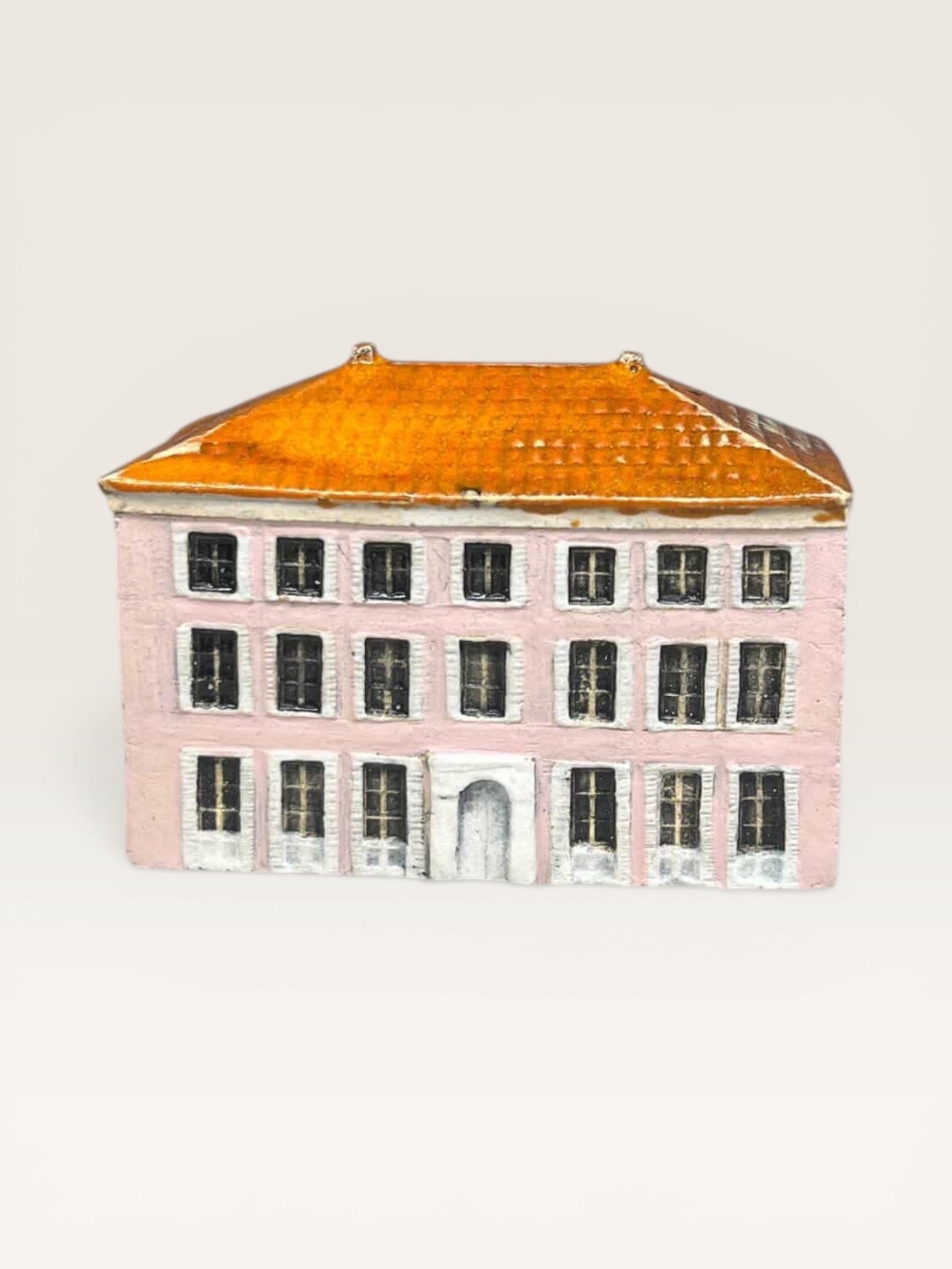 Front view of a handcrafted ceramic miniature house with a pink facade, glazed orange tile roof, and detailed white window frames.