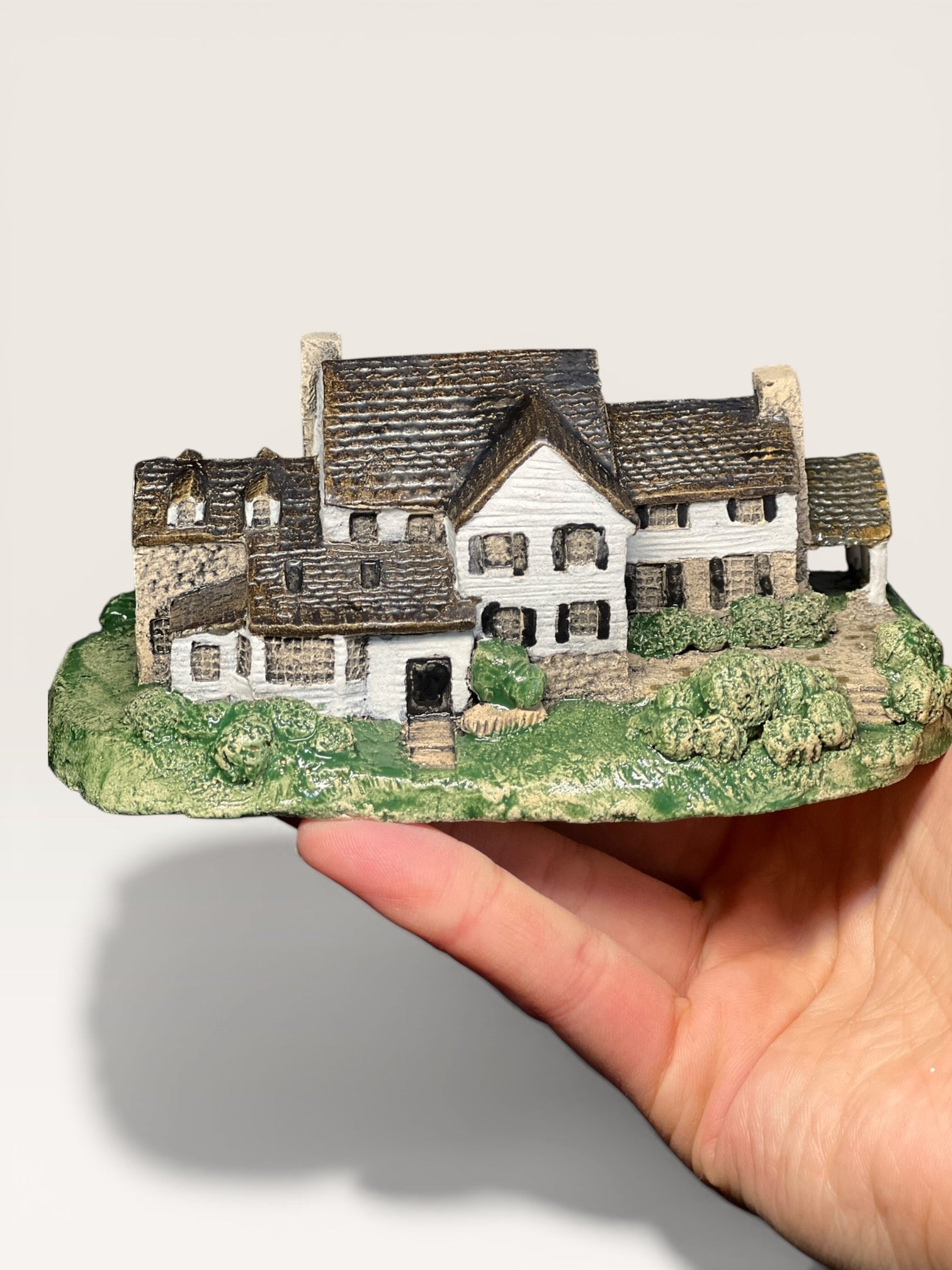 Handheld custom ceramic miniature of a stone country estate house with dormer windows and a green lawn base.