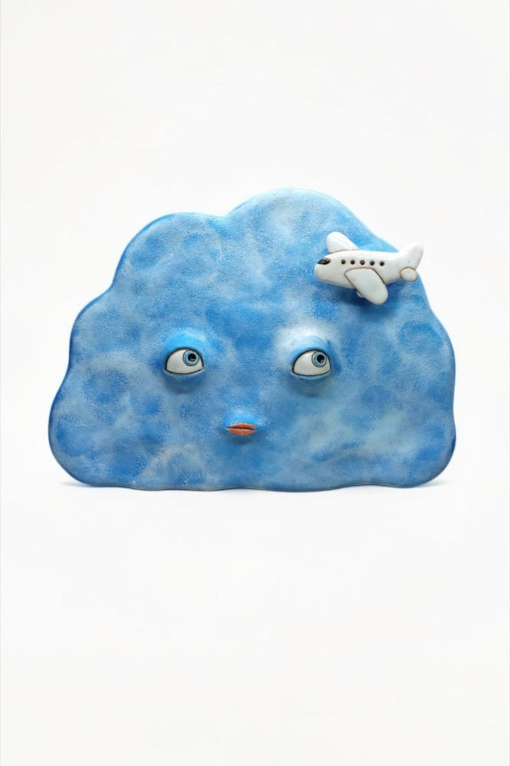 Artisan ceramic wall mask in the shape of a blue cloud with a small airplane, handcrafted from Sibelco stoneware.