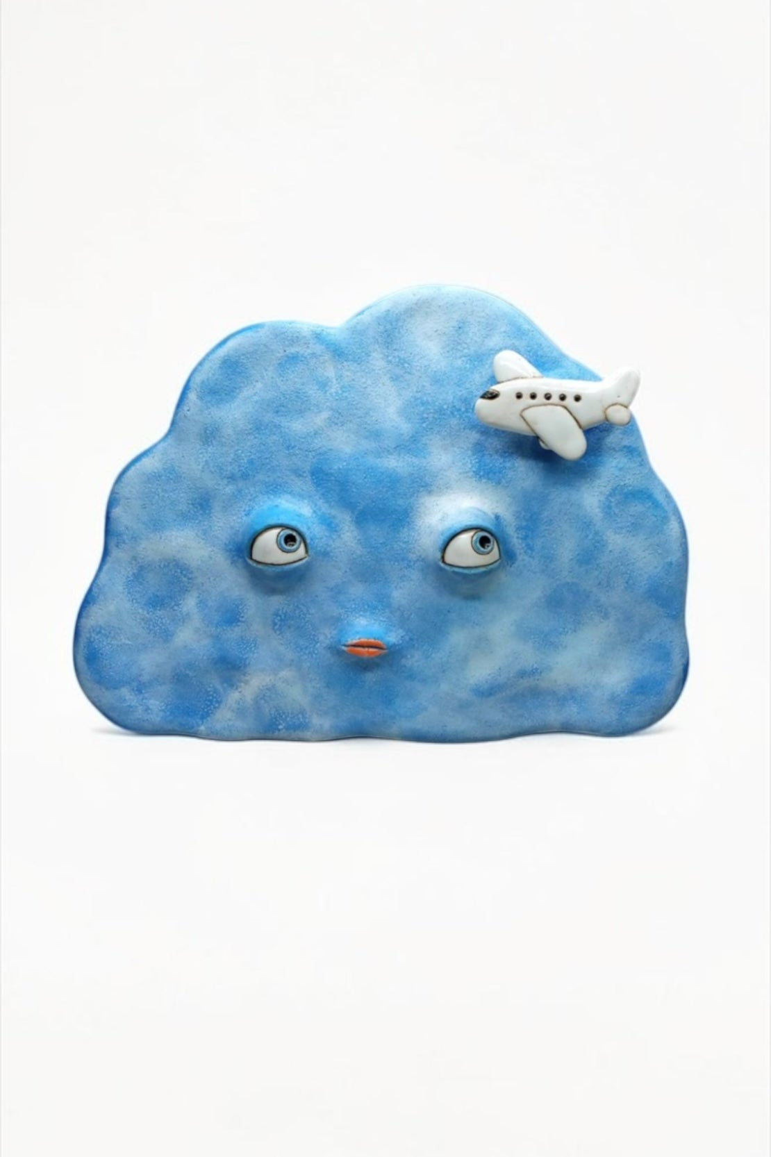 Artisan ceramic wall mask in the shape of a blue cloud with a small airplane, handcrafted from Sibelco stoneware.
