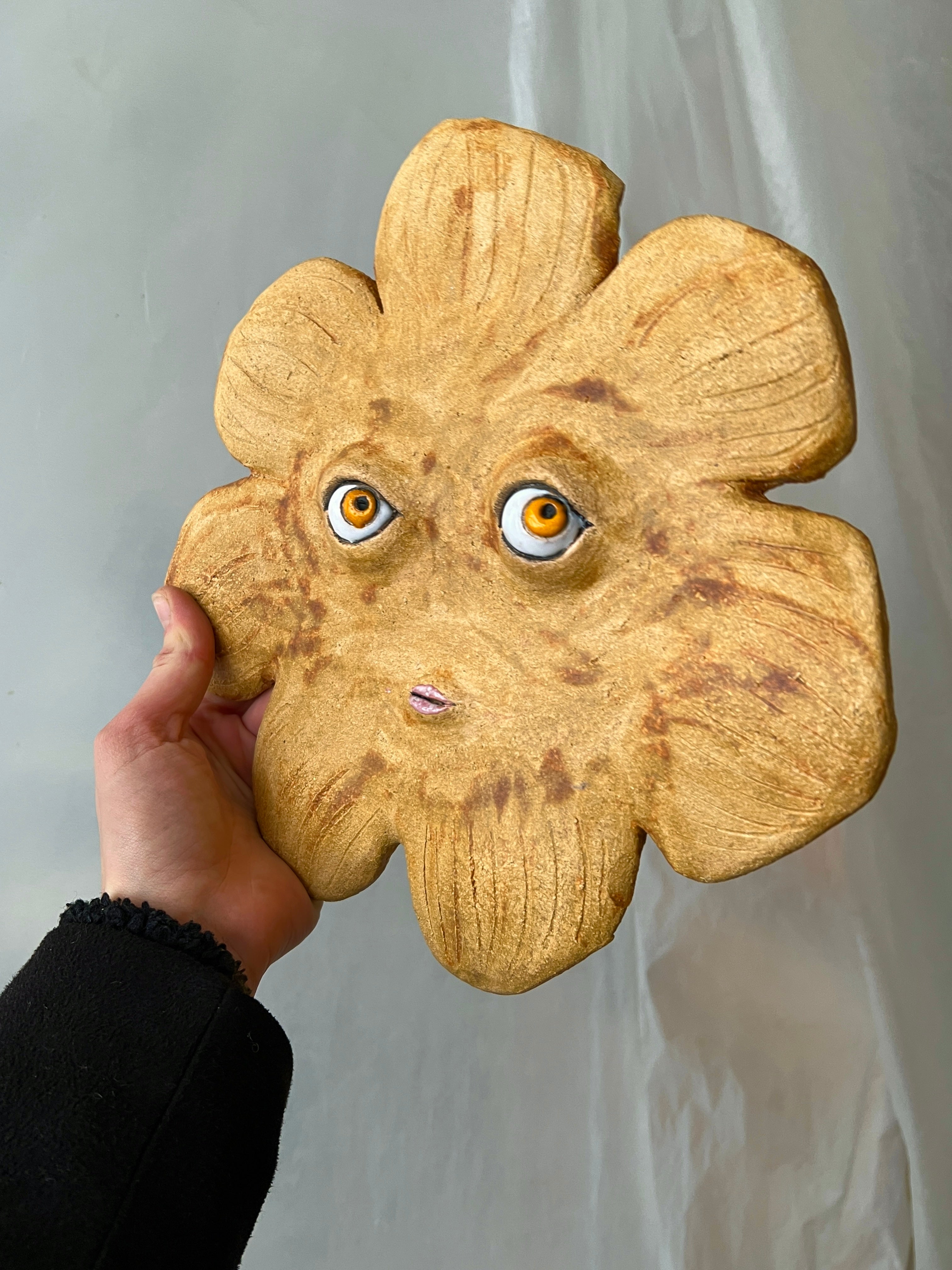 Handmade ceramic sun mask displayed on a gallery wall in a modern bright interior
